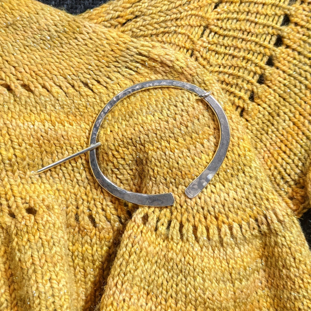 Sterling silver penannular shawl in with a hammered surface texture, pinning a yellow shawl shut.